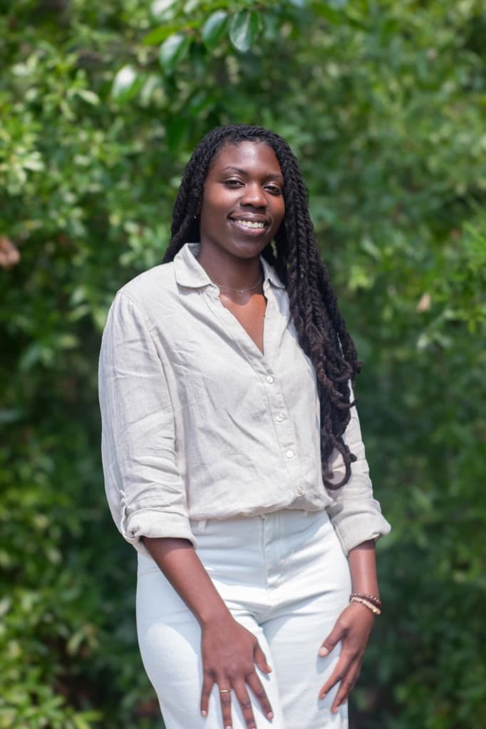 Church member smiling outdoors in front of green trees while wearing a light button-up shirt.