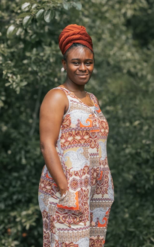 Church member standing outdoors in a patterned sleeveless dress and headwrap.