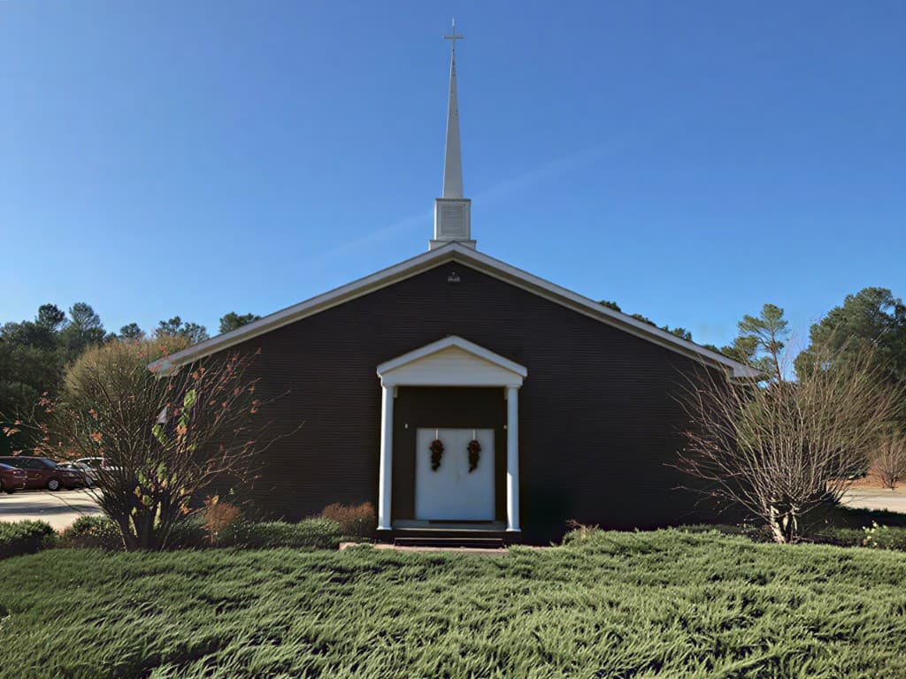 Fielding Spring Baptist Church exterior with white columned entrance, dark siding, and steeple against a blue sky